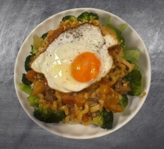 A photo of a white dish with layered with broccoli, pasta, bolognese sauce and fired egg.