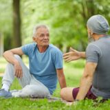 Two men is sitting on the grass in a park talking